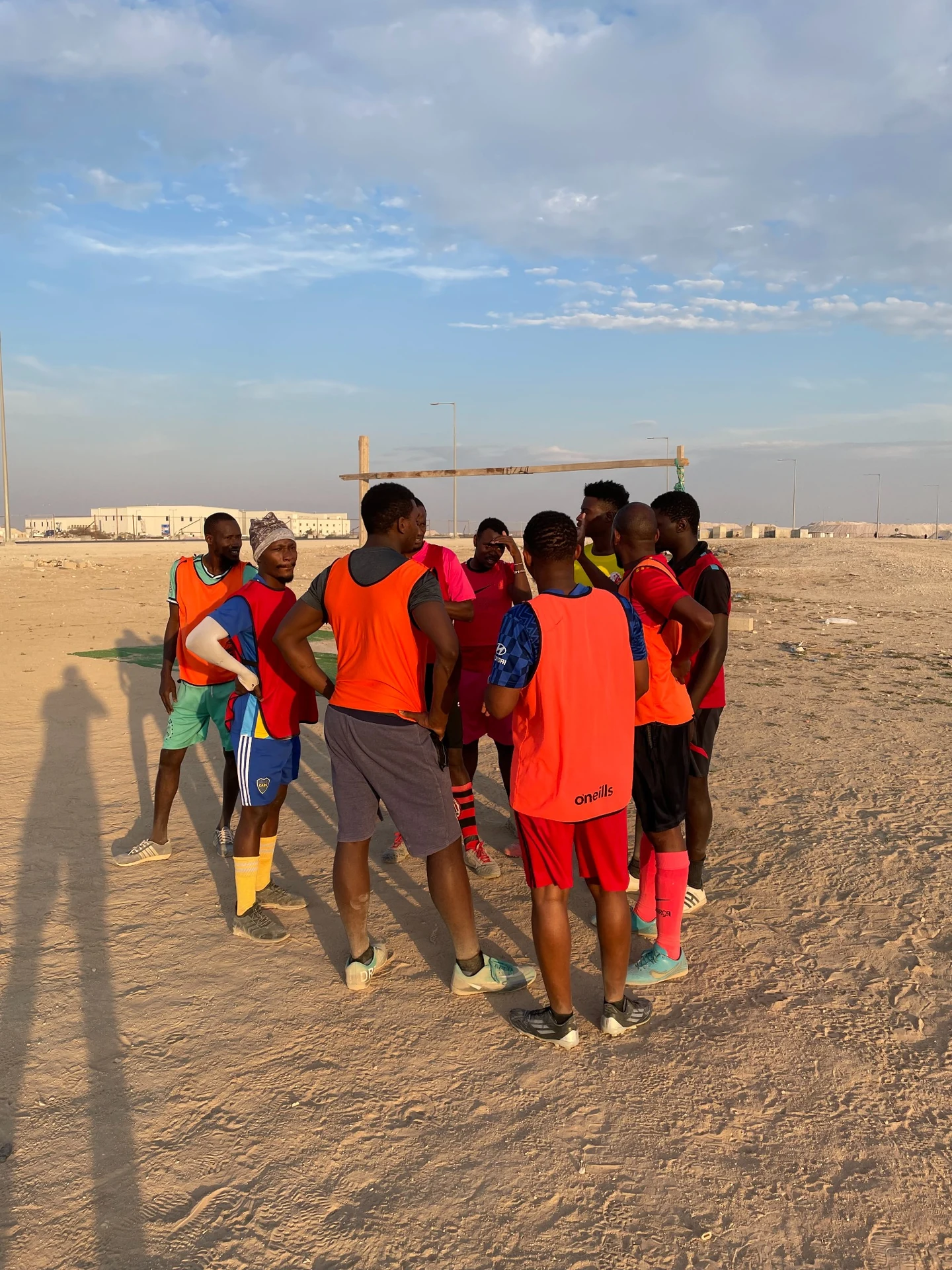 Footballers gathered in a huddle on a sandy pitch.