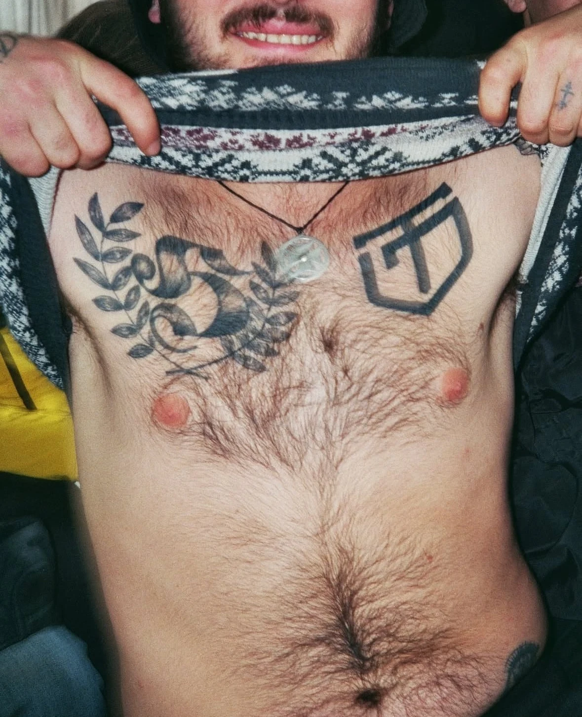 A supporter lifting his top to show chest tattoos.